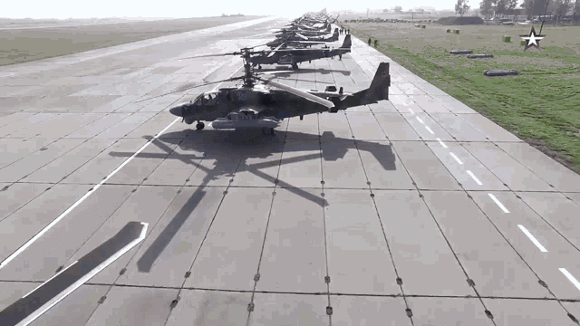 a row of military helicopters are parked on a runway with a red star in the background