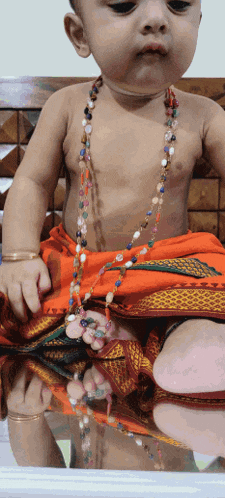 a baby wearing a necklace of beads sits on a couch