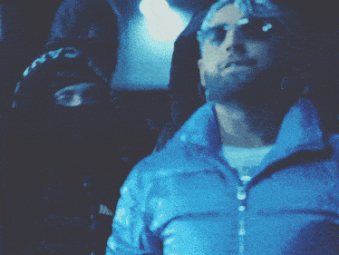 a man wearing sunglasses and a blue jacket is standing next to another man wearing a mask