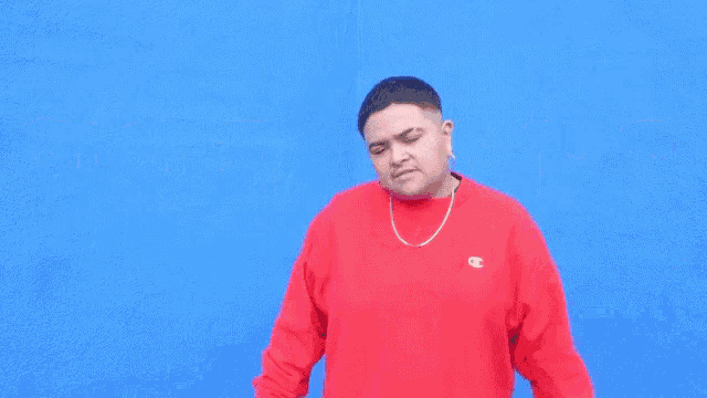 a man wearing a red champion sweatshirt is standing in front of a blue wall with yellow letters .
