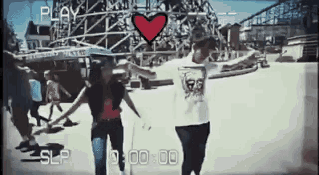 a couple holding hands in front of a roller coaster with a heart in the middle