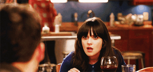 a woman sitting at a table with a glass of wine and a man behind her