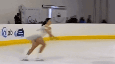 a woman is ice skating in front of a sign that says " iqlab "