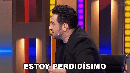 a man in a black suit is sitting in front of a microphone and says estoy perdidosimo