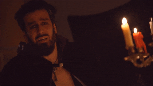 a man with a beard is standing in front of candles in a dark room