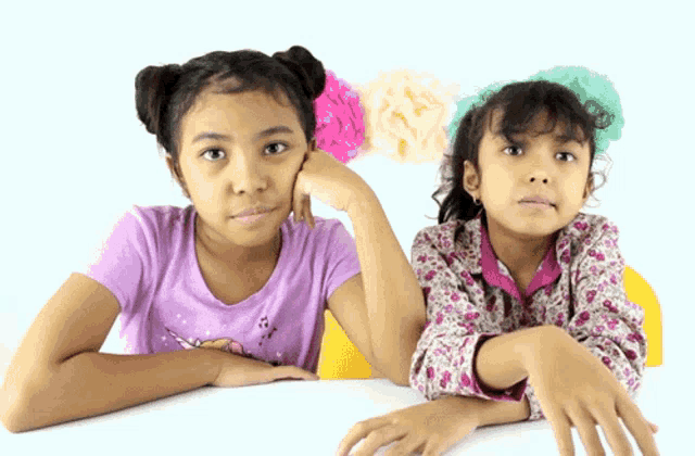 two little girls are sitting at a table with their arms crossed