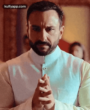a man with a beard and a white shirt is praying with his hands folded .