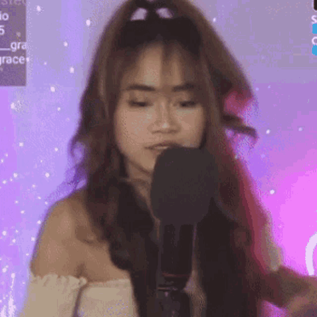 a woman is singing into a microphone with a purple background behind her