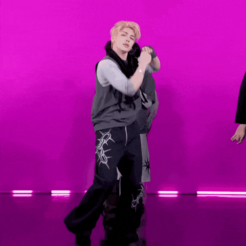a man in a gray vest and black pants is dancing in front of a purple background .