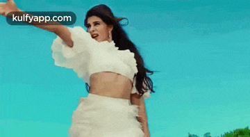 a woman in a white dress is standing in front of a blue sky with her hand in the air .