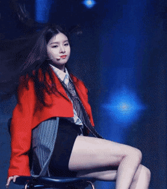 a woman wearing a red jacket and tie is sitting on a chair with her legs crossed