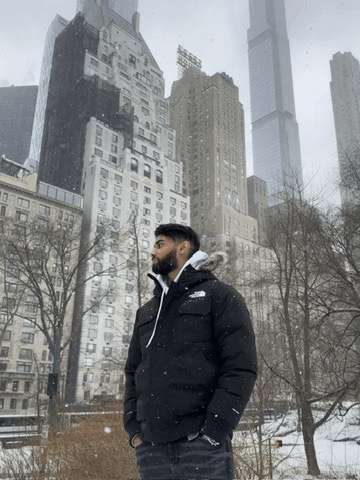 a man wearing a north face jacket stands in front of a snowy city skyline