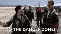 two men in military uniforms are standing next to each other on a runway with the words `` to the danger zone '' .