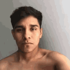 a shirtless man is taking a selfie while standing in front of a white wall .