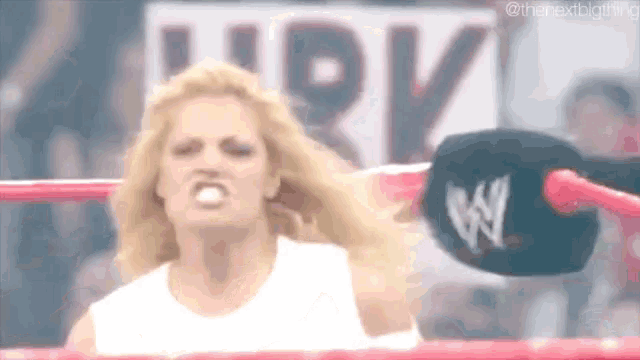 a woman in a white shirt is standing in a wrestling ring with her mouth open .