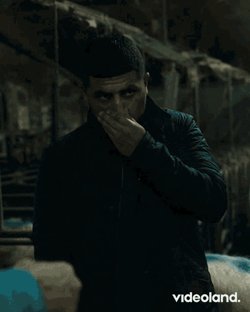 a man in a black jacket covering his mouth with his hand
