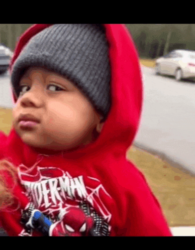 a little boy wearing a red superman shirt and a gray beanie