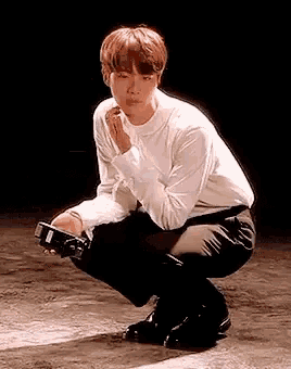 a young man in a white shirt and black pants is squatting down on a floor .
