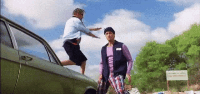 a man is jumping out of a car while another man stands next to him .