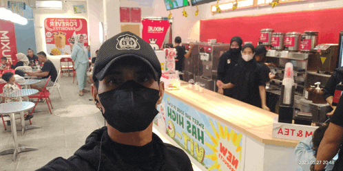 a man wearing a black mask stands in front of a sign that says mixu