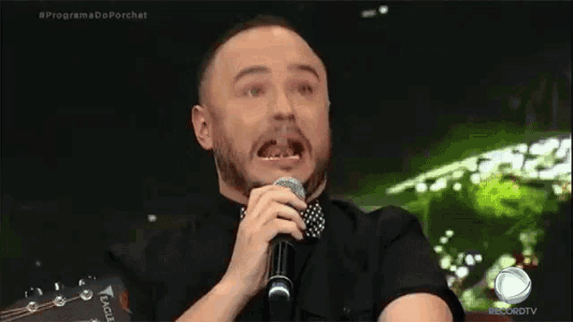 a man with a beard is singing into a microphone with his mouth open .