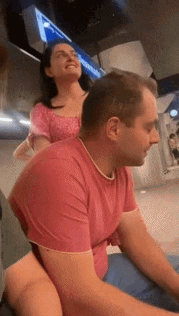 a woman in a pink top sits on the back of a man