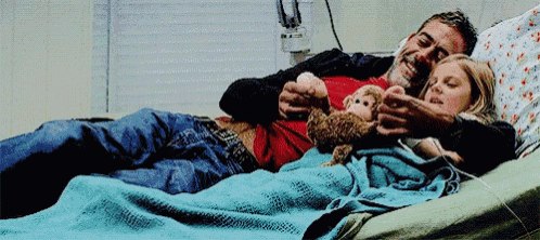 a man and a little girl are laying in a hospital bed holding a teddy bear .
