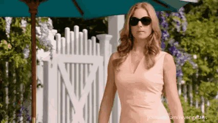 a woman wearing sunglasses is standing under an umbrella