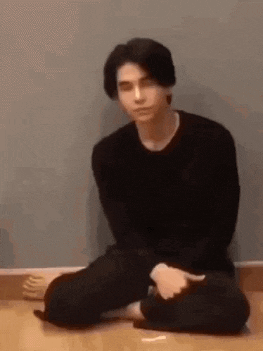 a young man is sitting on the floor with his legs crossed and looking at the camera .