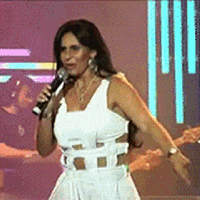 a woman in a white dress is singing into a microphone on a stage