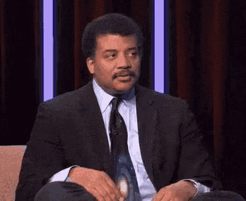 a man in a suit and tie is sitting in a chair and making a funny face .