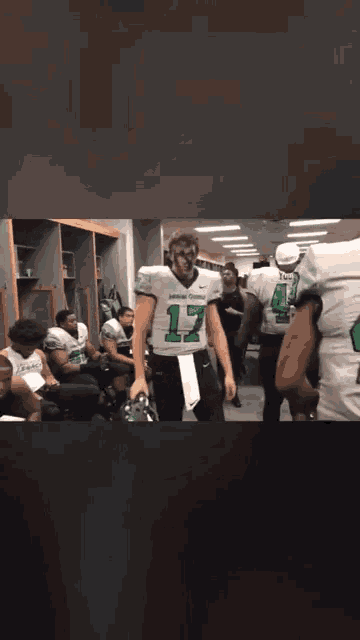 a football player with the number 17 on his jersey stands in a locker room
