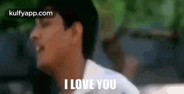 a man in a white shirt is saying `` i love you '' while standing in front of a car .