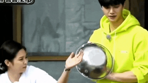 a man in a neon yellow hoodie is holding a bowl in his hands while a woman looks on .