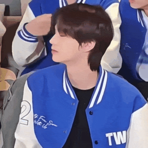 a young man wearing a blue and white baseball jacket is sitting in a room .