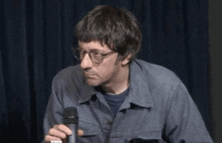 a man wearing glasses and a blue jacket is holding a microphone in his hand .