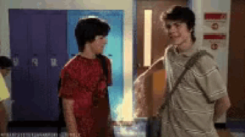 two boys are standing next to each other in a hallway in front of blue lockers .