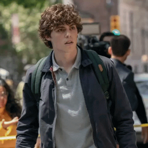 a young man with curly hair and a backpack is walking down a city street .