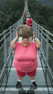 a man in a pink shirt holds a large rock over his head
