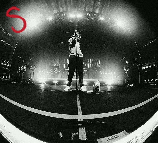 a black and white photo of a man singing into a microphone with a red letter s in the corner