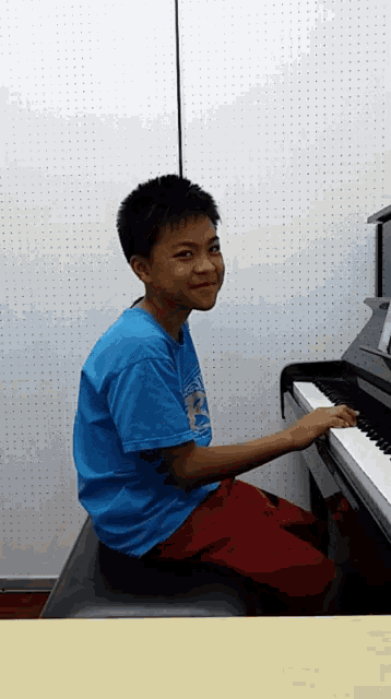 a boy in a blue shirt with the letter p on it sits at a piano