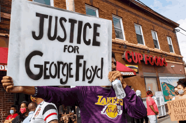 a man in a purple lakers shirt holds a sign that says justice for george floyd
