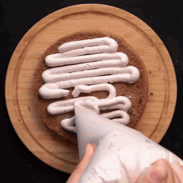 a person is piping whipped cream on a cake on a wooden plate