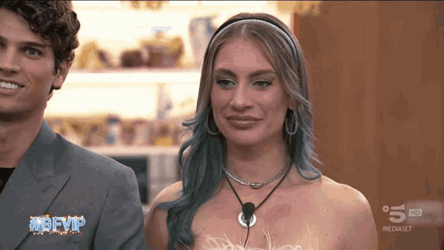 a woman with blue hair is standing next to a man on a television screen that says ' mgfvip '