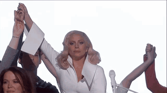 a woman in a white dress is surrounded by people holding their hands up