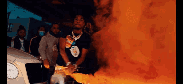 a man in a black shirt with the word fendi on it stands in front of a fire