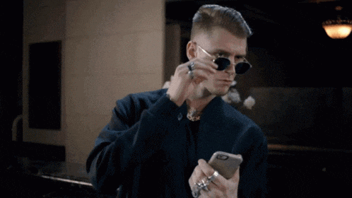 a man wearing sunglasses and rings is looking at his phone