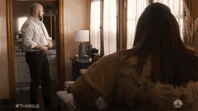 a man and a woman are standing in a living room with #thisisus written on the bottom right