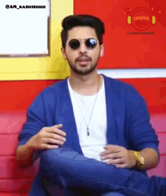 a man wearing sunglasses and a blue jacket sitting on a couch