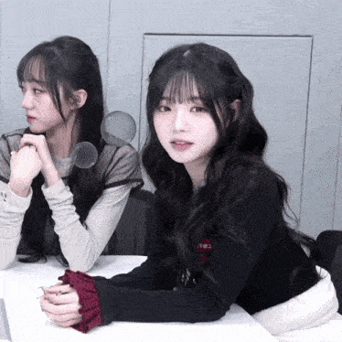 two girls are sitting at a table with one wearing a black sweater that says " i love you "